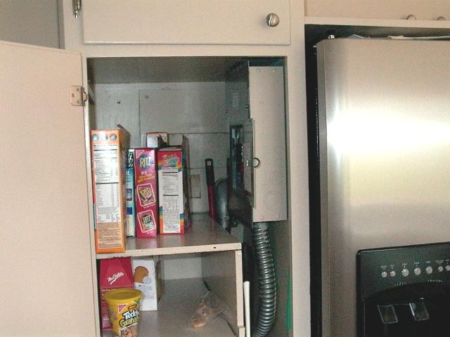 a pantry closet with full shelves in front of 
	the wall containing an electrical panel cover.