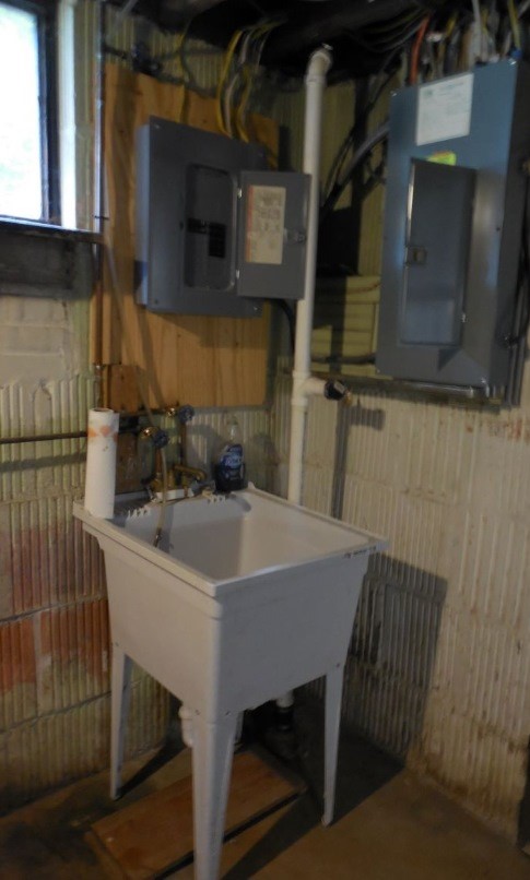 A white washtub sitting in a corner, below 
	circuit breaker panels.